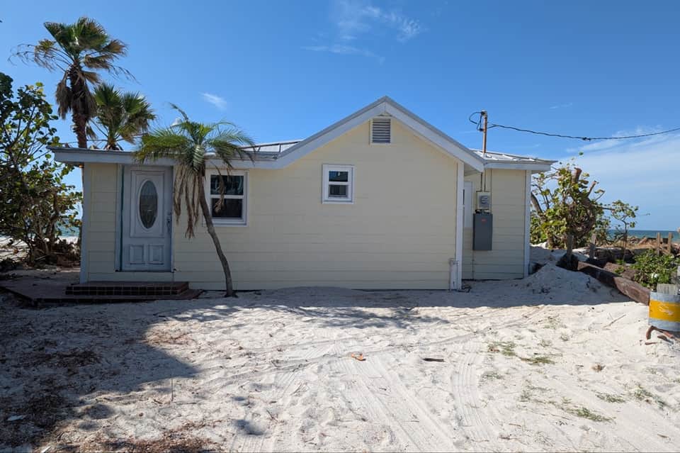 Beachfront cottage with cream siding, palm trees, and ocean view beyond