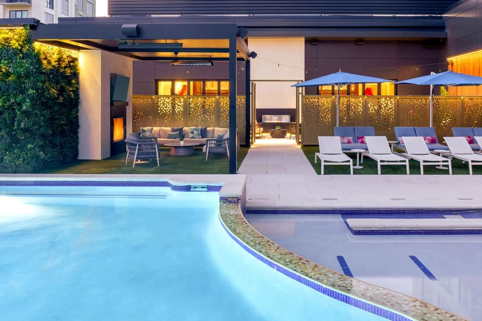 Illuminated resort pool deck at dusk with lounge chairs, fire pit, and covered seating areas