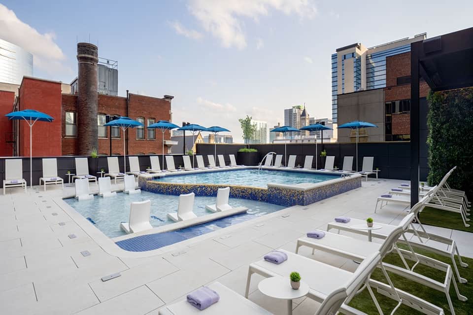 Modern rooftop pool with blue umbrellas, lounge chairs, and city skyline views