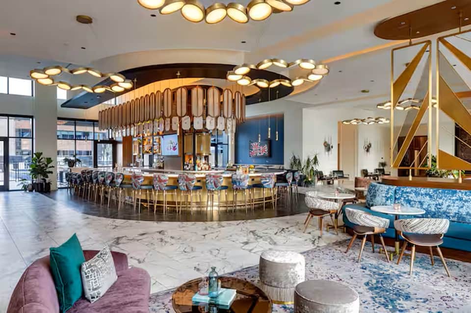 Modern hotel bar and lounge with gold lighting fixtures, colorful seating, and spiral staircase