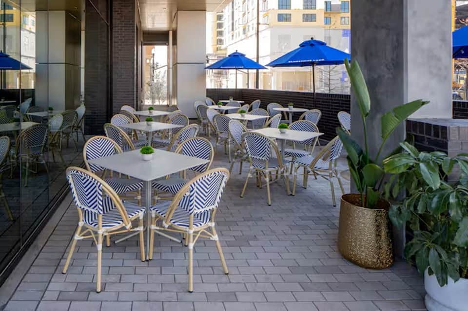 Rooftop dining area with blue umbrellas, patterned chairs, white tables, and potted plants