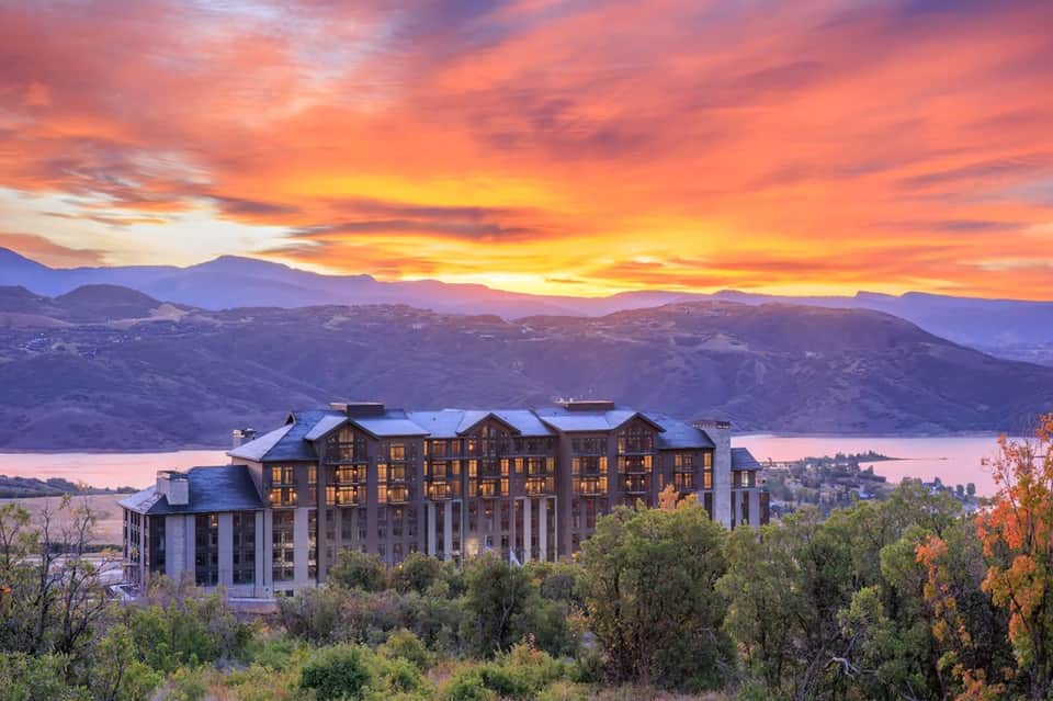Upscale resort building at sunset with illuminated windows overlooking a lake and mountains at dusk