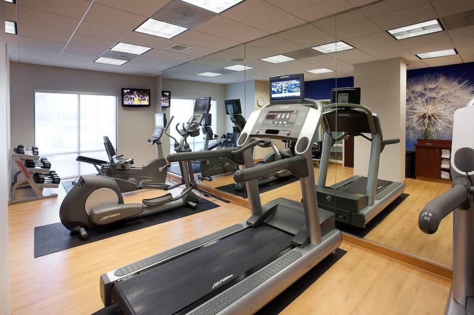 Fitness center with treadmills, elliptical machines, and dumbbells reflected in mirror wall