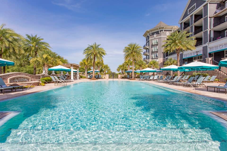 Resort pool surrounded by teal umbrellas, palm trees, and residential buildings on waterfront