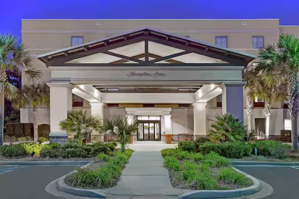 Hampton Inn hotel entrance with white columns, dark roof, and manicured landscaping at dusk