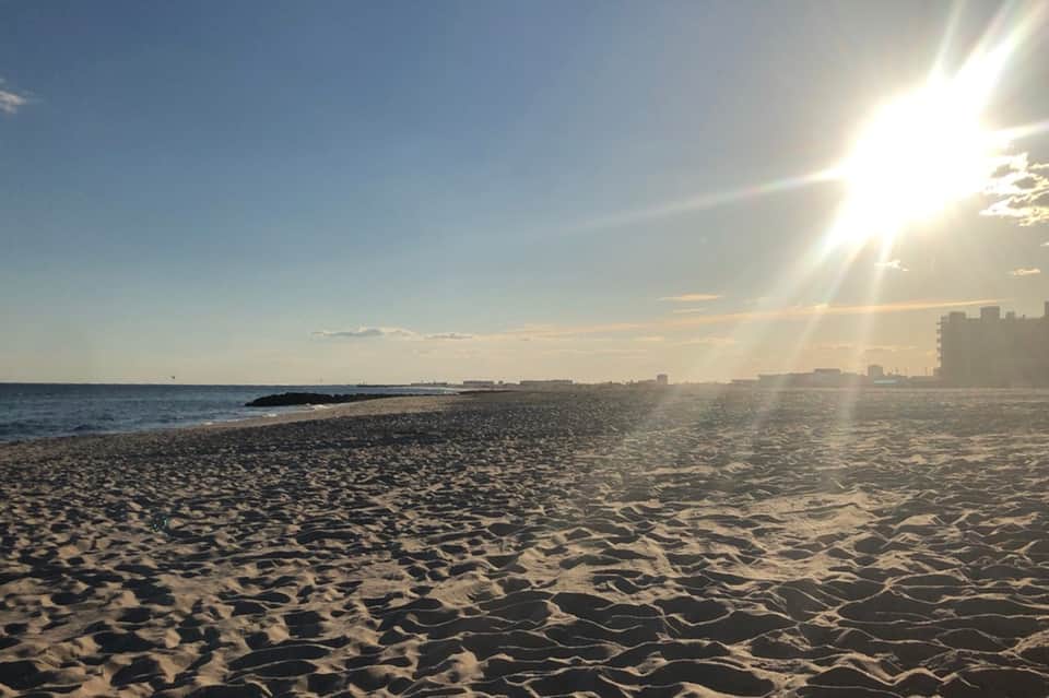 Sandy beach at golden hour with calm ocean and coastal buildings in background