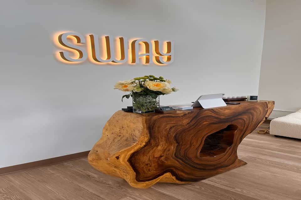 Modern hotel lobby entrance with illuminated 'sway' signage and natural wood reception desk