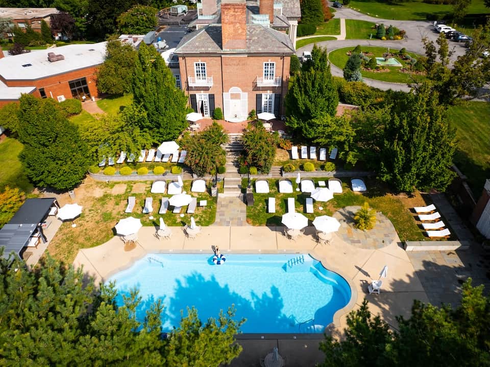 Aerial view of brick mansion with curved pool and white lounge chairs