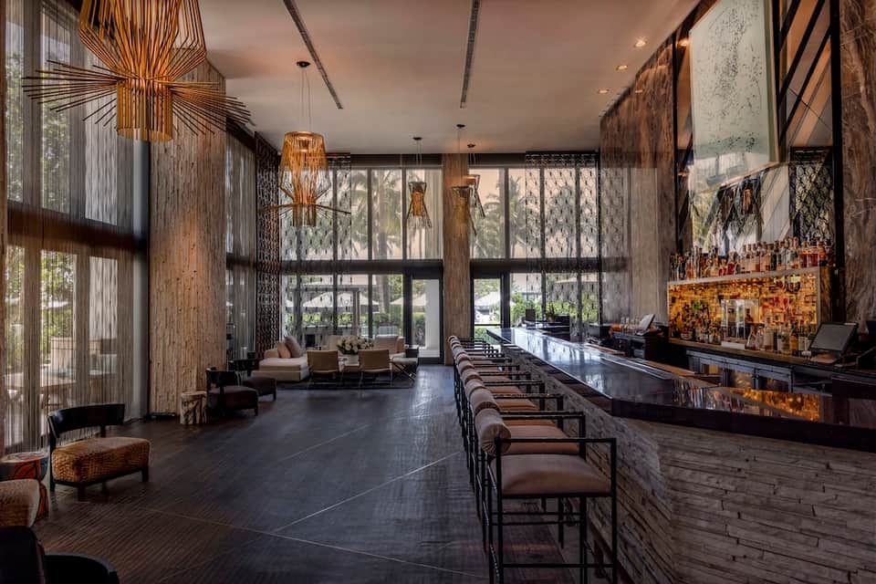 Contemporary hotel lobby lounge with gold pendant lights, dark bar, high windows, and seating area