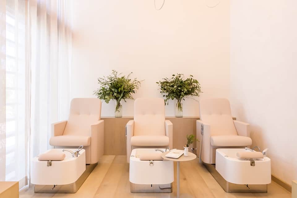 Spa pedicure area with three white massage chairs and fresh flower arrangements on wood tables