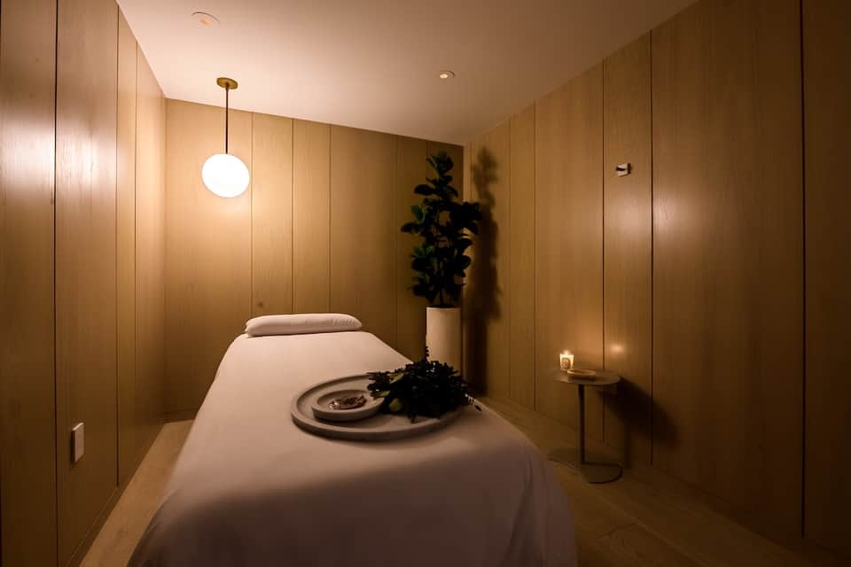Minimalist spa treatment room with wooden walls, massage table, and modern pendant lighting