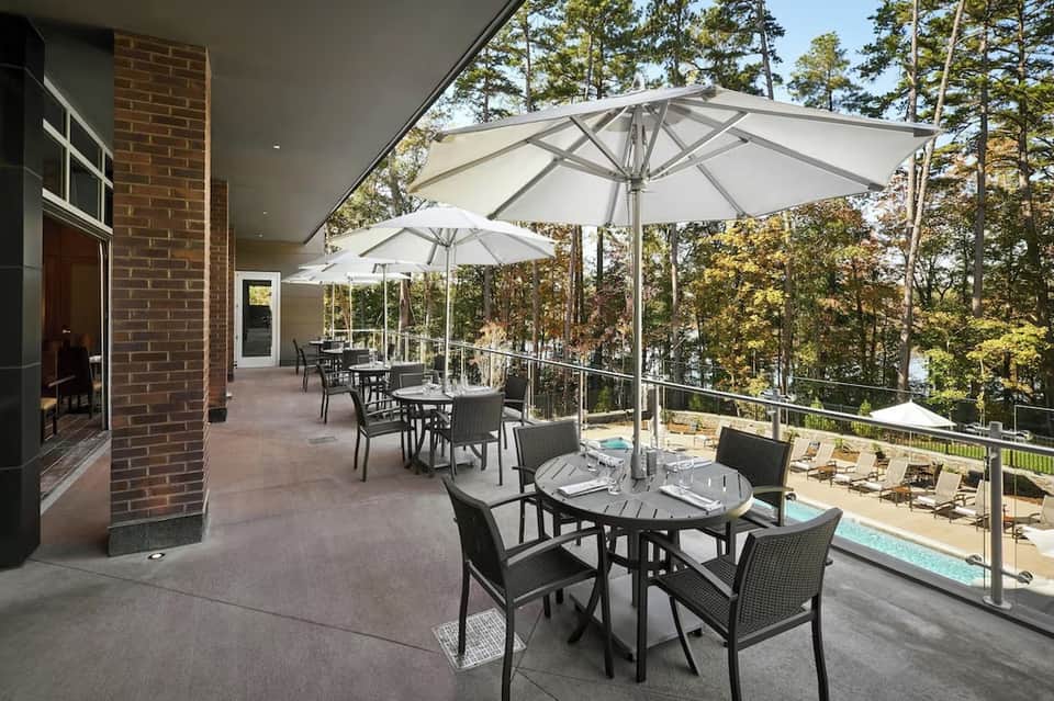 Elevated patio with white umbrellas, dining tables, and pool views through trees