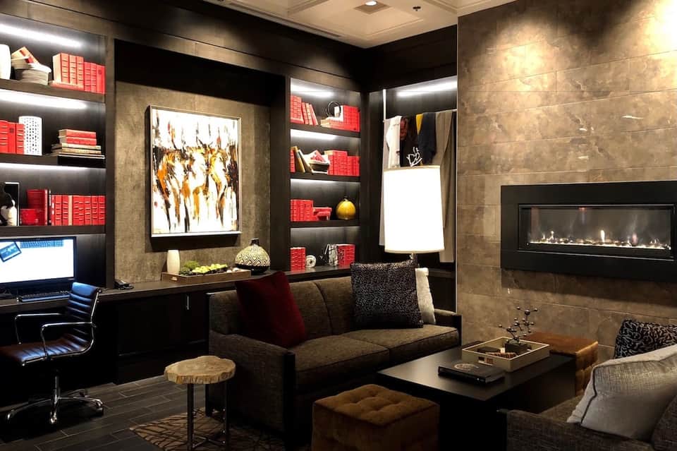Luxury office lounge with fireplace, red-accented shelving, artwork, and modern seating