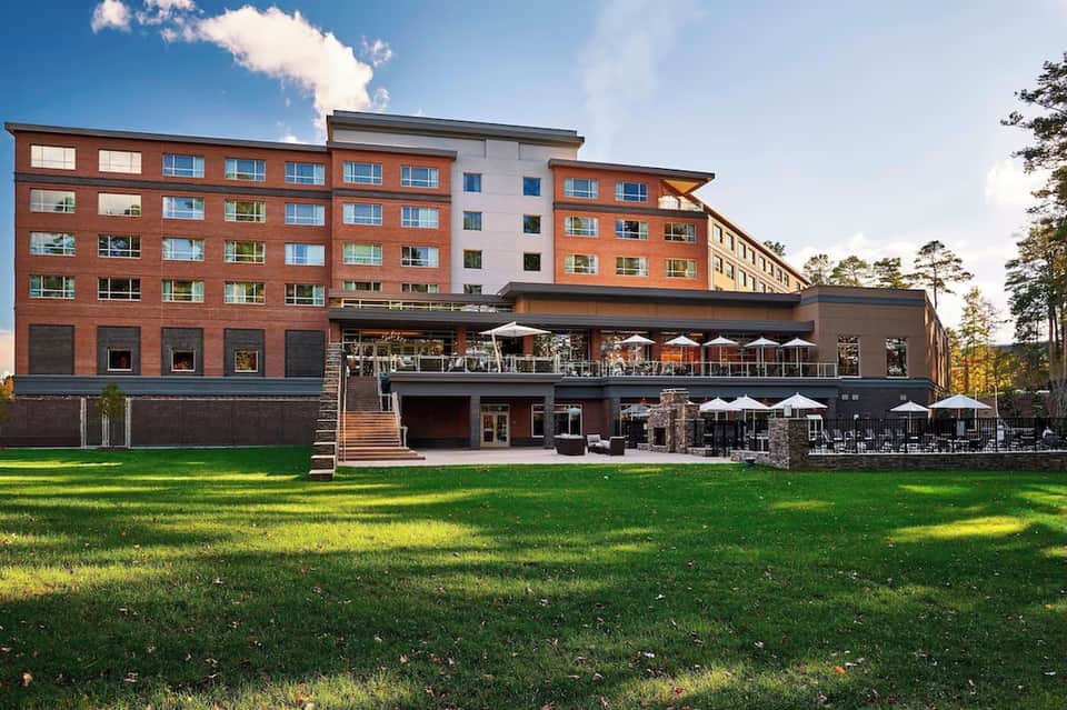 Multi-story resort building with red brick facade, expansive lawn, and outdoor dining terrace