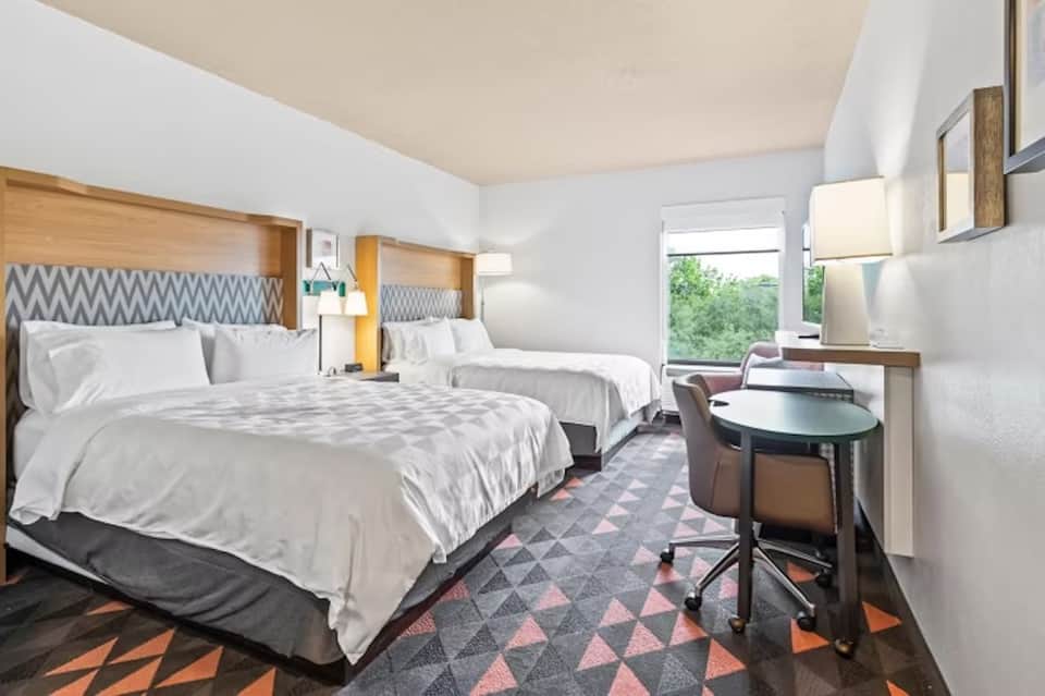 Modern hotel bedroom with two queen beds, geometric patterned headboards, and work desk