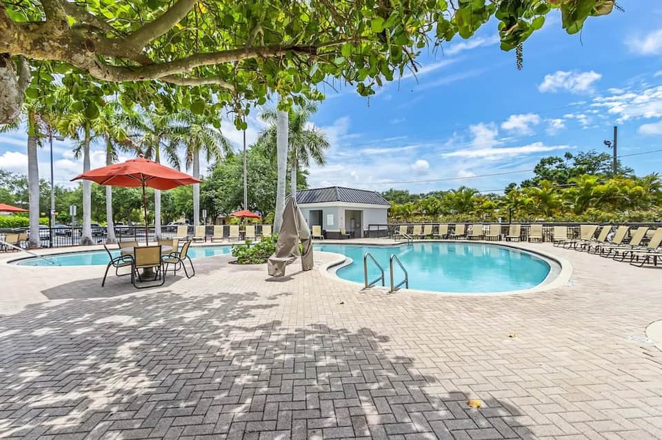 Resort courtyard with dual pools, red umbrellas, lounge seating, and mature palm trees