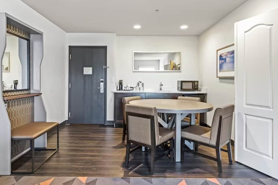 Hotel suite interior with round dining table, kitchenette, and entry door