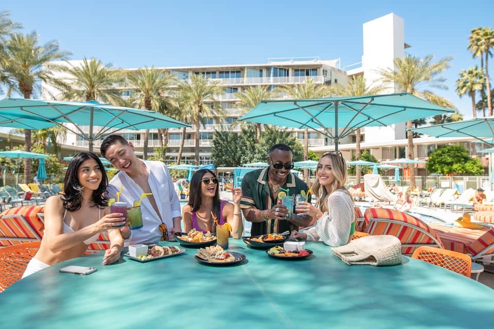 Beachfront resort guests enjoying cocktails under turquoise umbrellas with palm trees