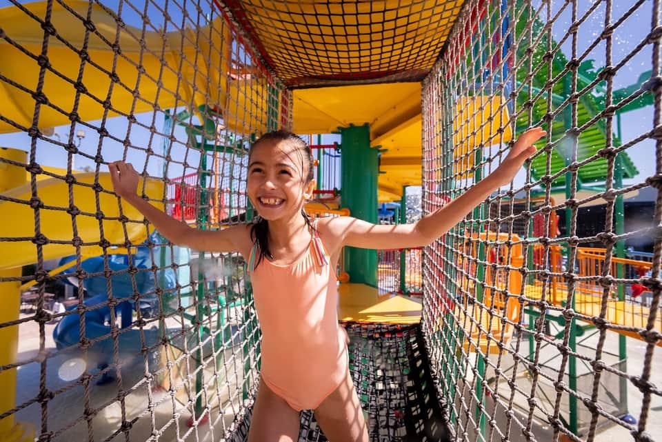 Young child enjoying a colorful indoor play structure with netting and bright primary-colored panels