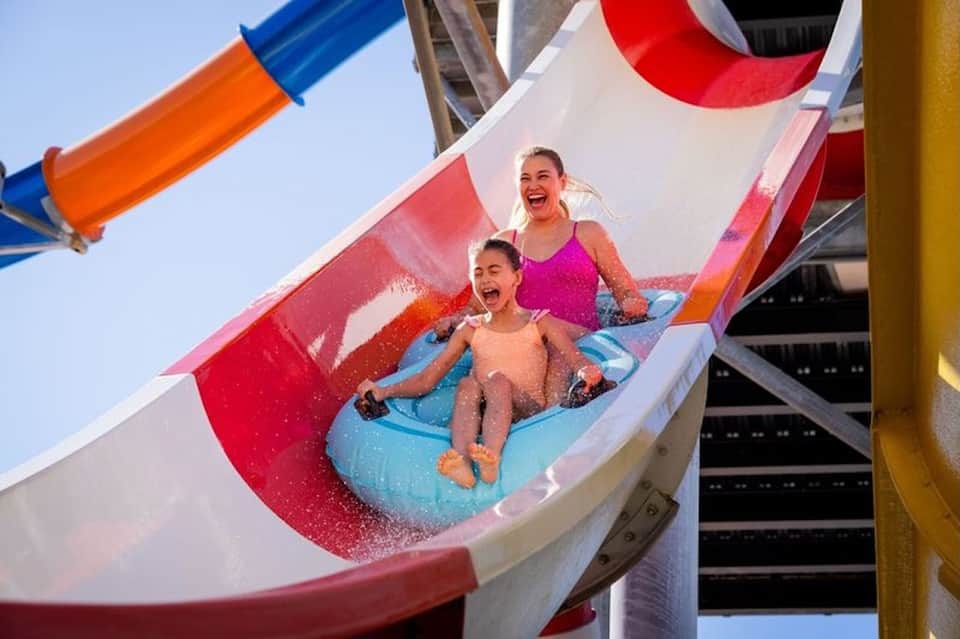 Children on colorful water slide at resort with red and white slide, clear blue sky