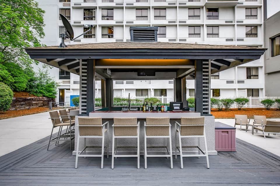 Contemporary poolside bar with modern pergola, woven bar stools, contemporary seating, and hotel building backdrop