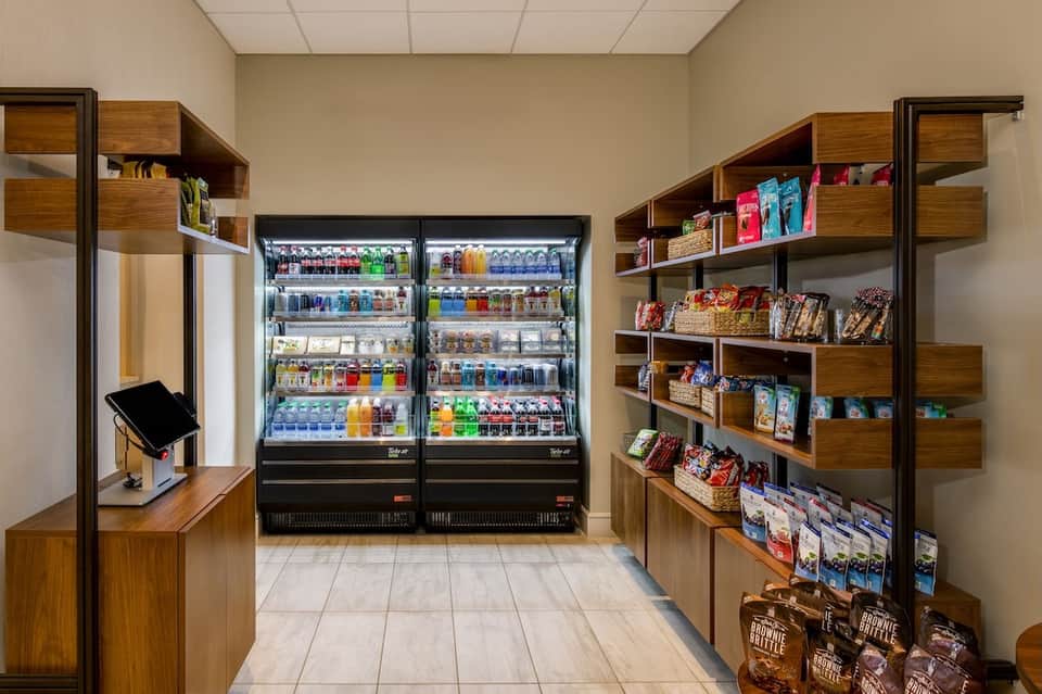 Convenience shop interior with refrigerated beverage cases and wooden shelving units stocked with snacks