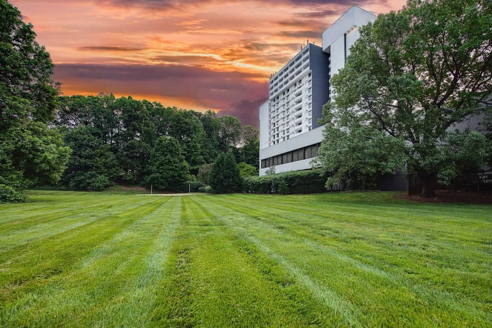 Modern hotel building at sunset with manicured lawn and tree line at dusk