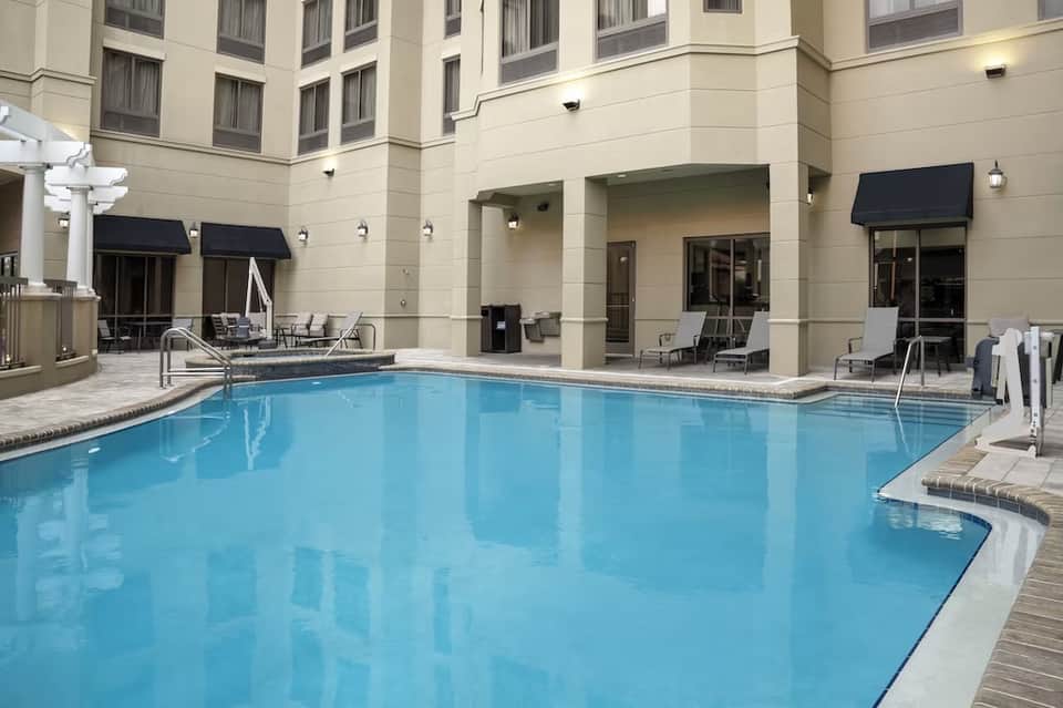 Indoor hotel pool with calm blue water, surrounding lounge chairs, hotel rooms, and covered patio area