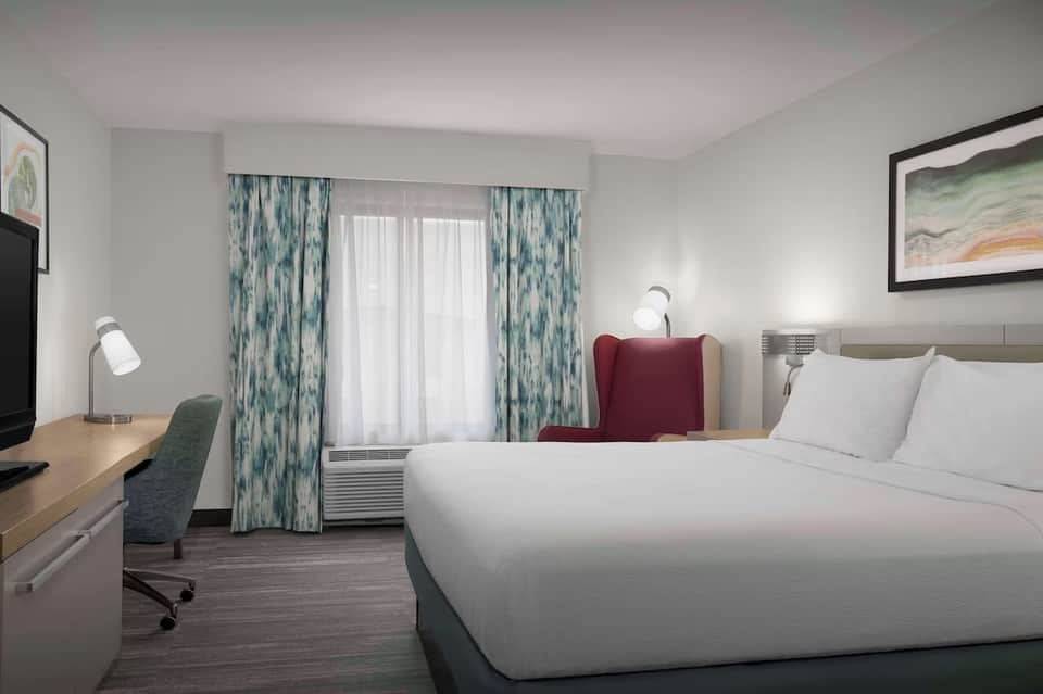 Modern hotel bedroom with queen bed, desk, patterned curtains, and flat-screen TV