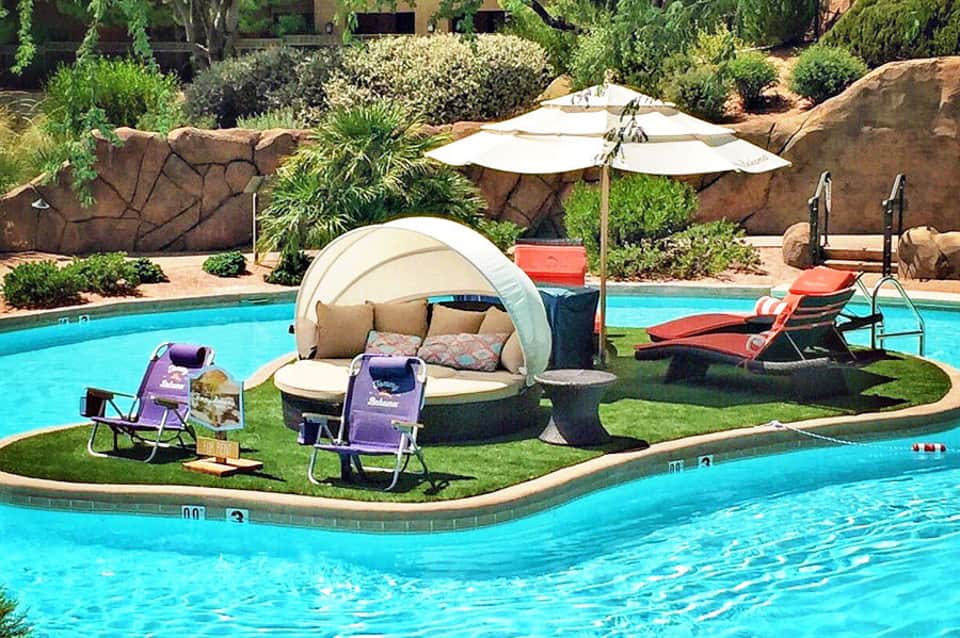 Resort pool area with turquoise water, lounge chairs, cabana with canopy, umbrellas, and manicured landscape