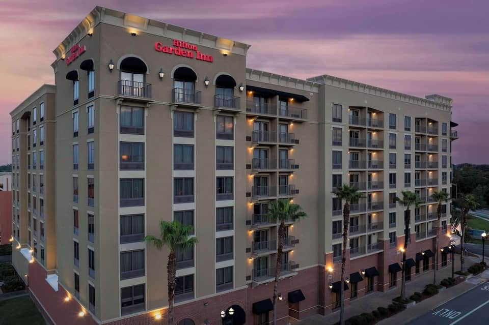 Hilton Garden Inn hotel exterior at dusk with illuminated facade and palm trees