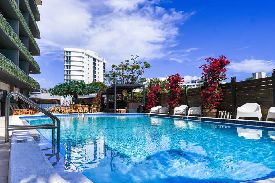 Resort outdoor pool with blue water, white loungers, red flowering vines, and modern building facade