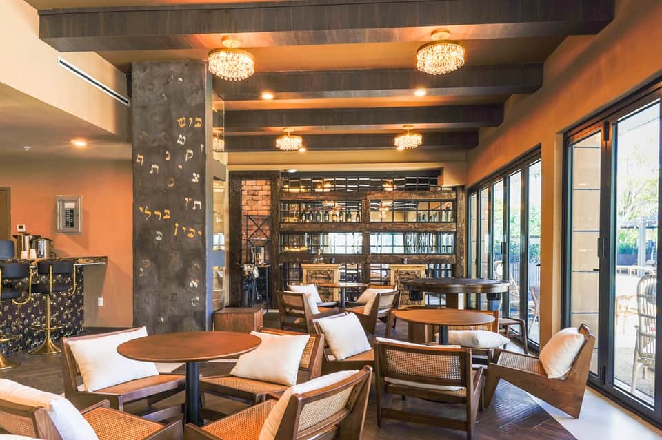 Upscale lounge area with orange walls, crystal chandeliers, wooden furnishings, and glass doors to patio