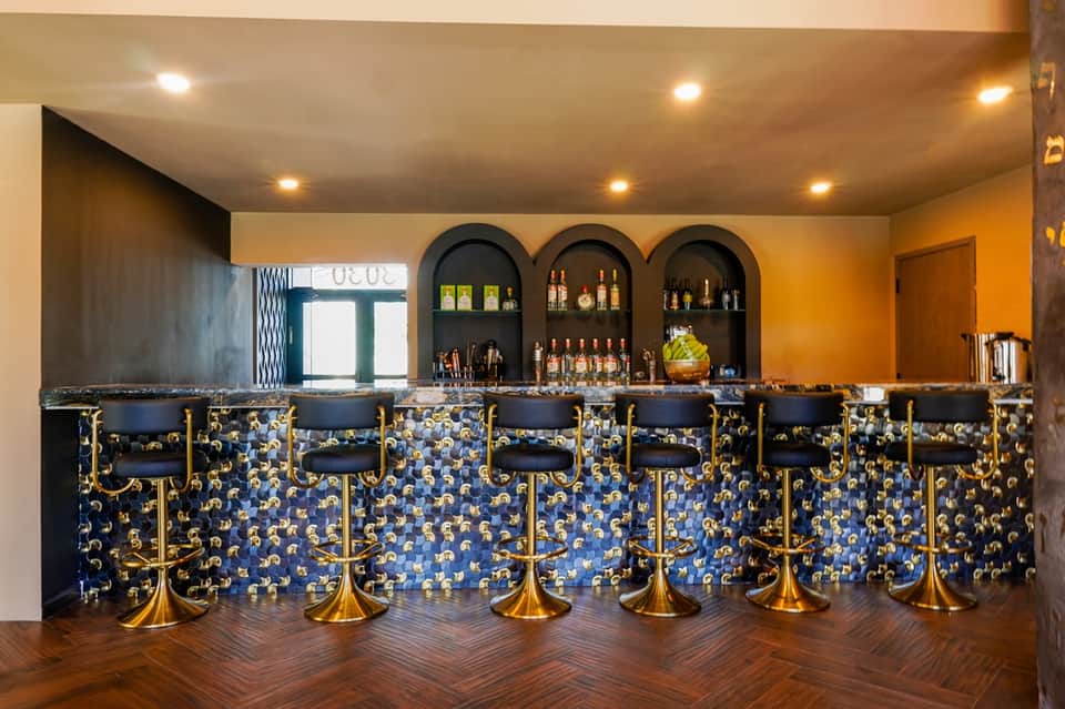 Upscale bar with arched alcoves, blue-patterned backsplash, gold-trimmed chairs, and warm lighting.