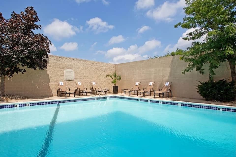 Rectangular pool with lounge chairs against tan walls under blue sky