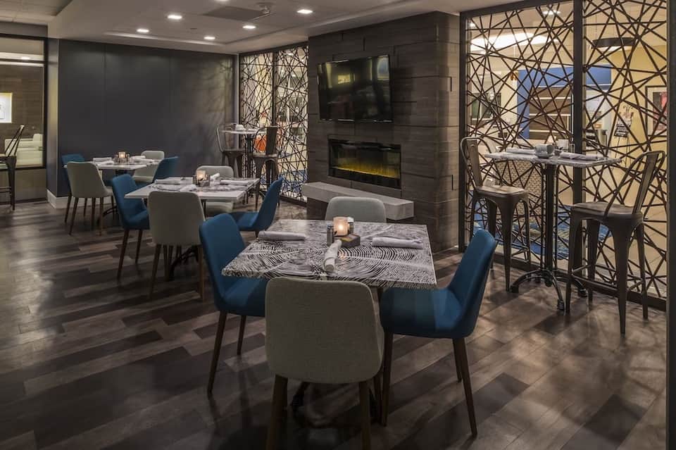 Contemporary dining room with blue chairs, patterned tables, fireplace, geometric window screens