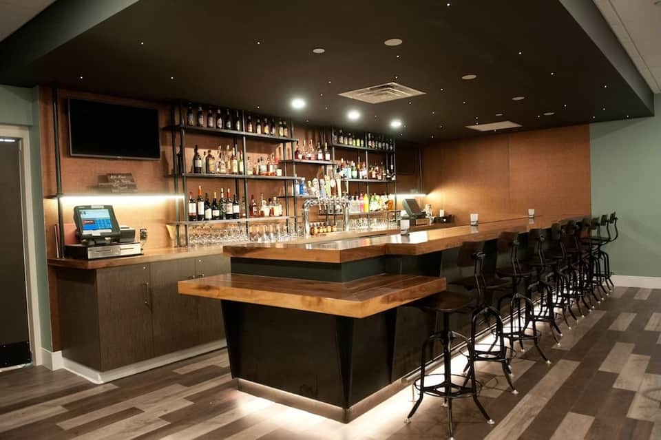Contemporary bar with wood top, shelving display of liquor bottles, and black bar stools