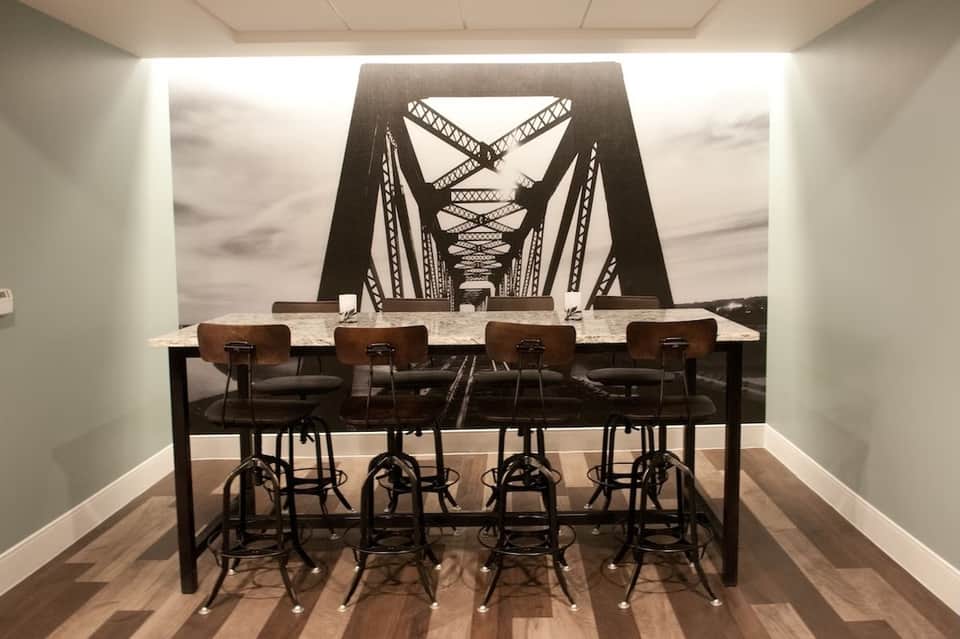 Conference room with high-top marble table, industrial-style chairs, and bridge mural