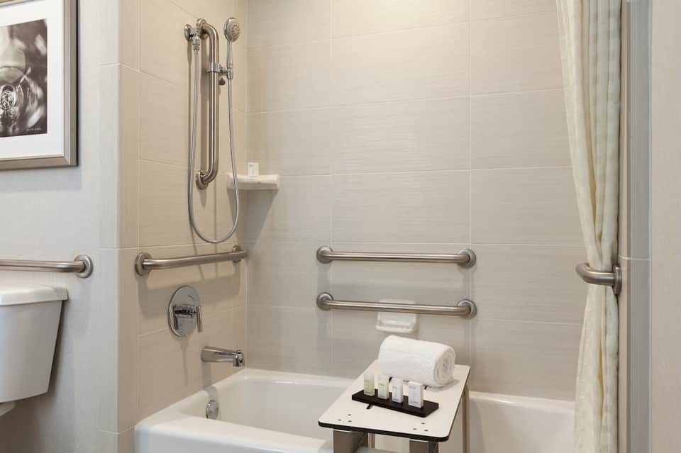 Accessible bathroom with grab bars, walk-in shower, and white tiled walls with safety features