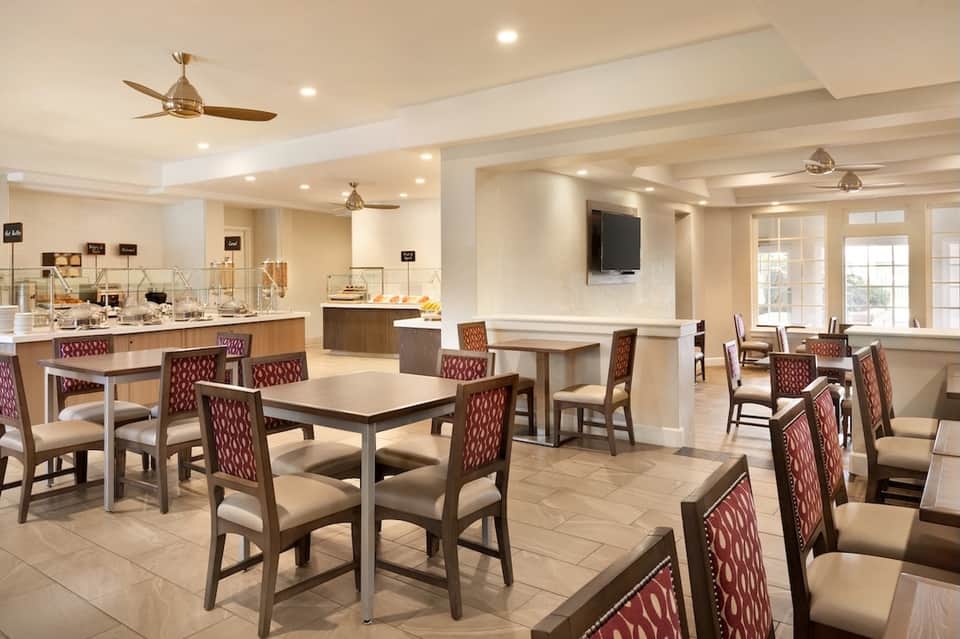 Casual dining area with multiple tables, burgundy chairs, buffet station, and flat-screen TV