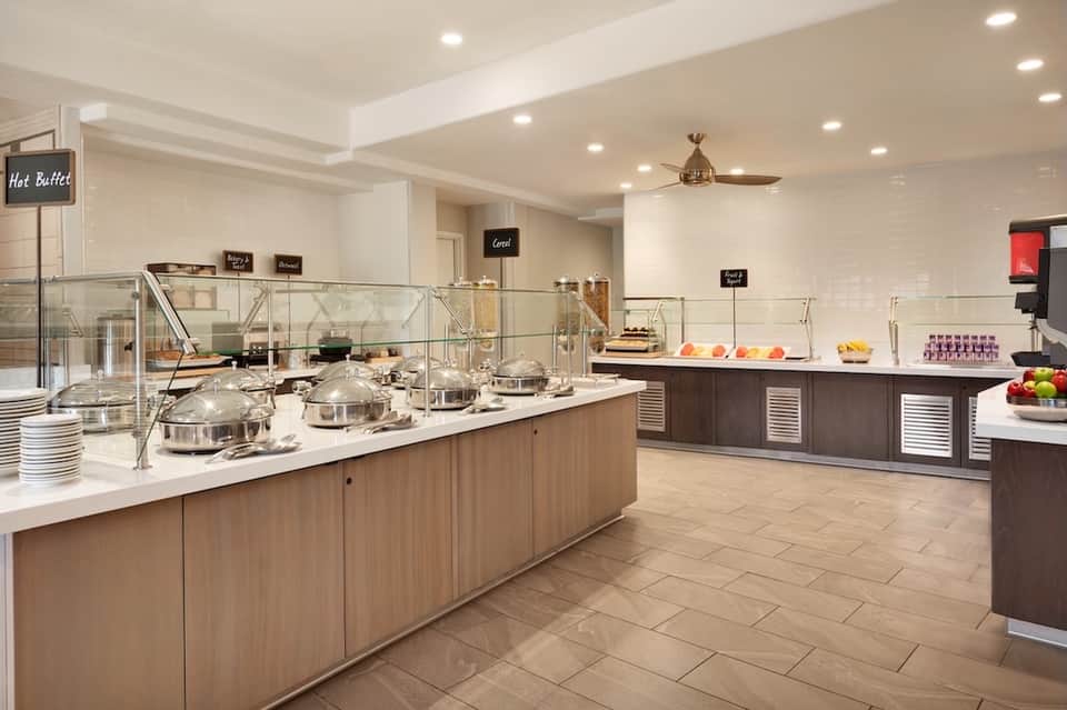 Breakfast buffet area with white tile floor, serving stations, and fresh fruit displays