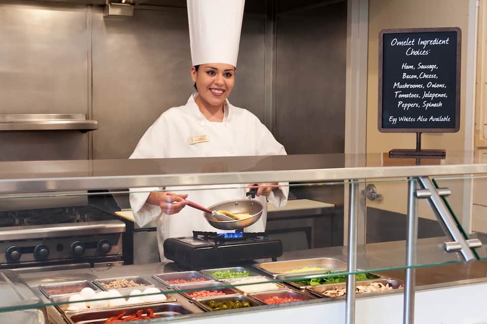 Chef in white uniform preparing omelets at open kitchen counter with ingredient display