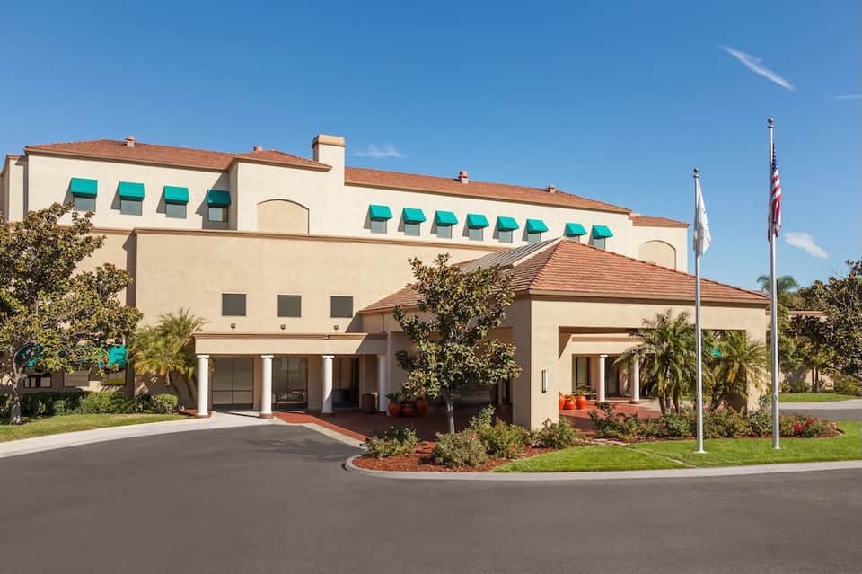 Hotel exterior with beige stucco facade, turquoise awnings, and manicured landscaping