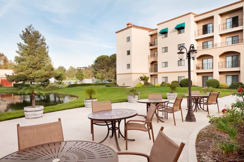 Hotel exterior with patio seating overlooking pond and manicured green lawn