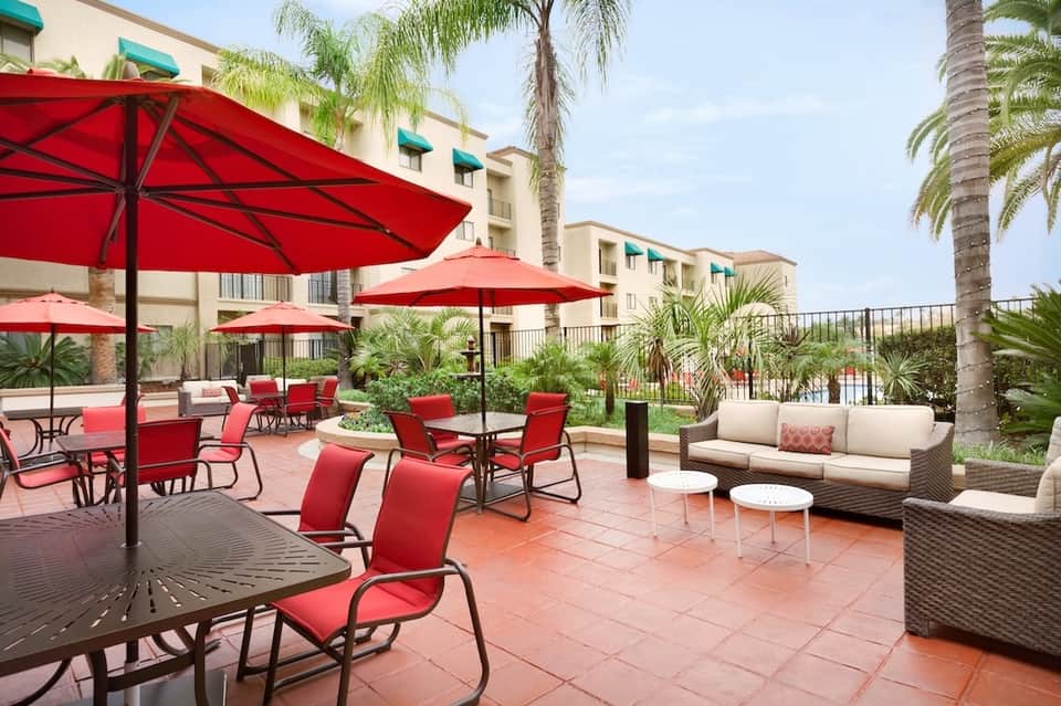 Resort courtyard with red umbrellas, lounge seating, and tropical palm tree landscaping