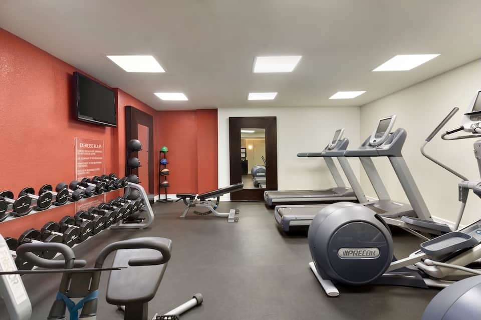 Fitness center with red accent wall, dumbbells, treadmills, and exercise equipment