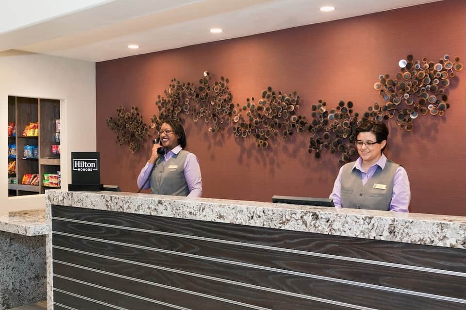 Hotel front desk with two staff members in uniforms, marble counter, and decorative wall art
