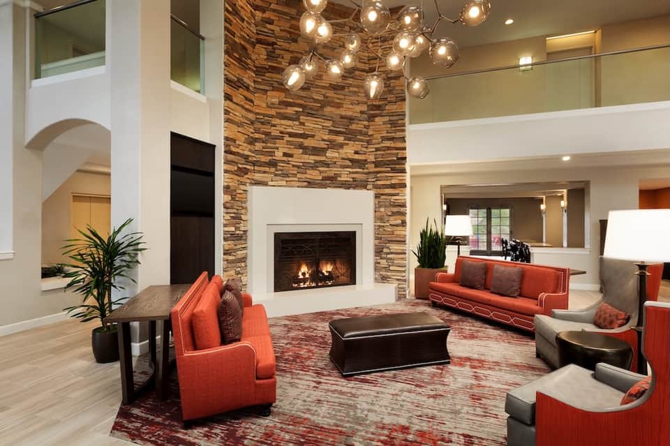 Upscale hotel lobby with fireplace, stone accent wall, orange seating, and pendant lights