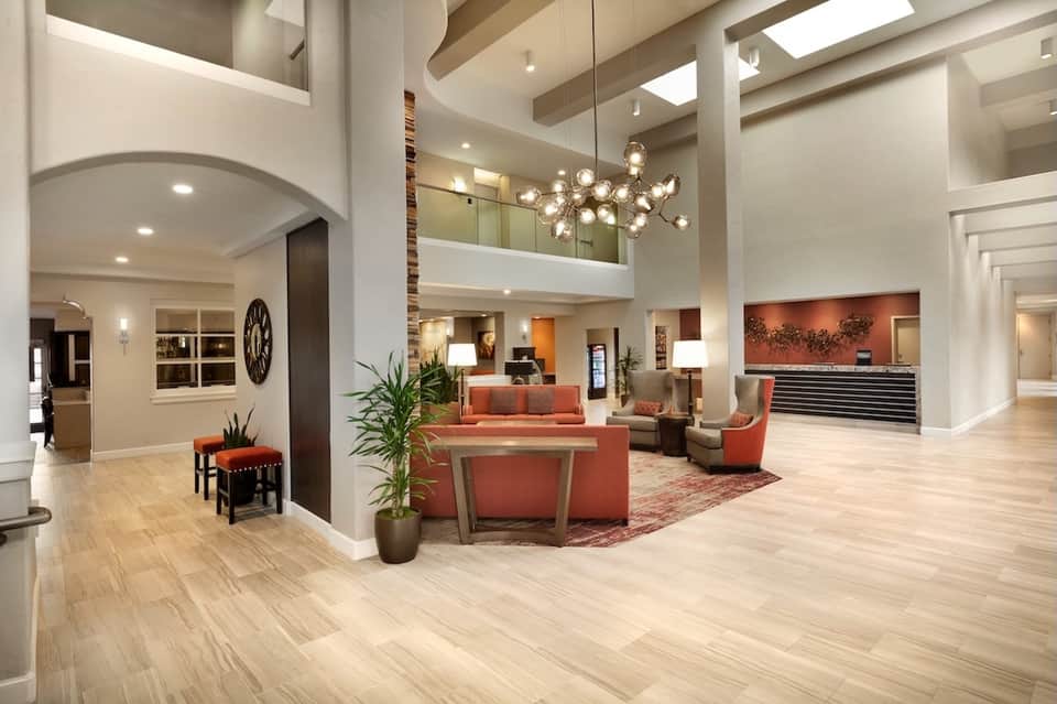 Spacious hotel lobby with high ceilings, modern chandelier, coral accent furniture, and open floor plan