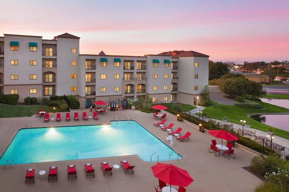 Modern hotel building with pool surrounded by red lounge chairs and umbrellas at twilight